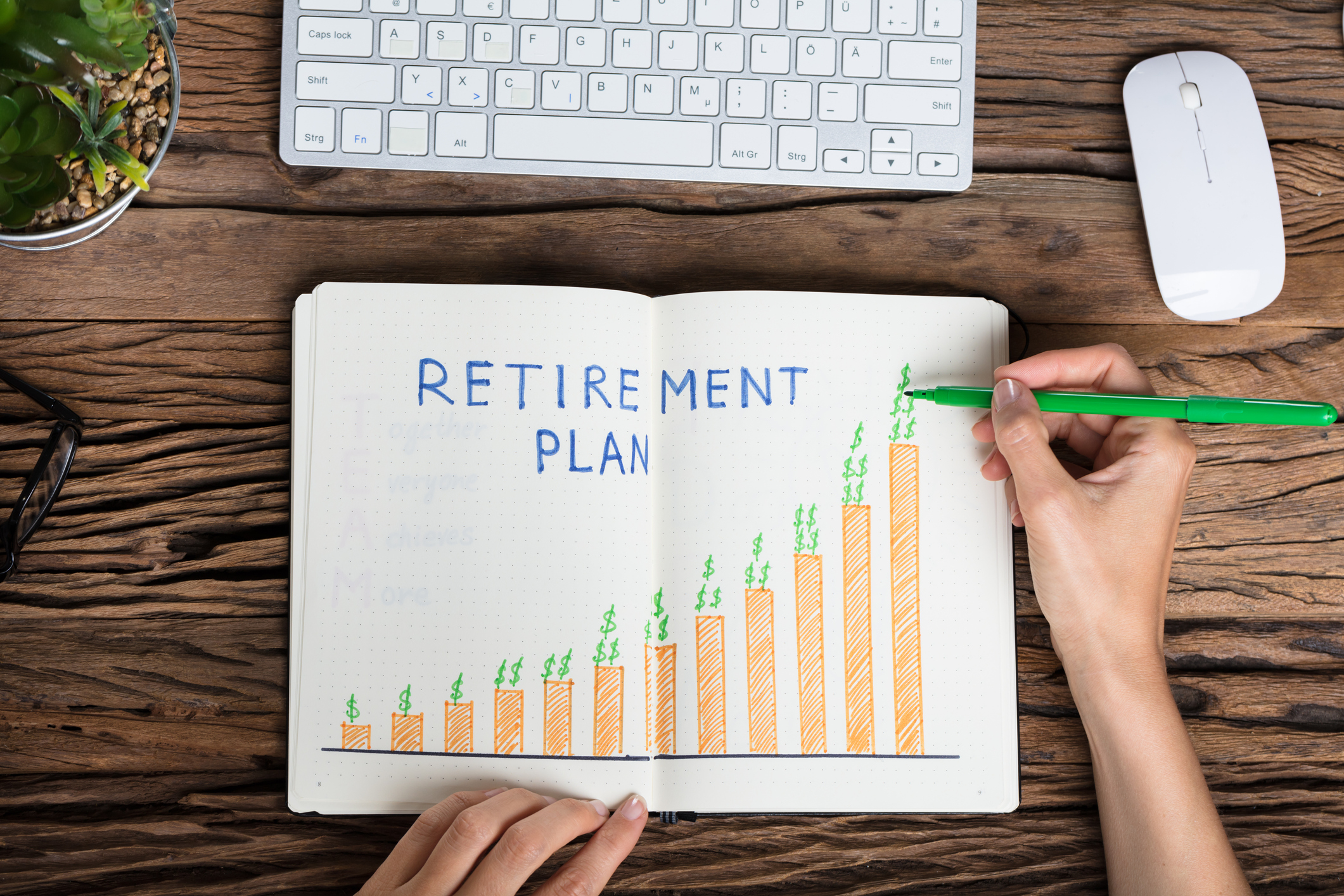  A person drawing a graph in a notebook with the words 'Retirement Plan' written at the top while holding a green marker.